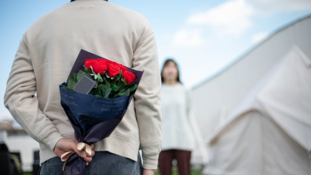 後ろ手に赤い花を持ち、女性の前に立つ男性の後ろ姿