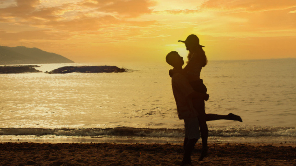 夕日の海で女性を抱き上げる男性